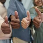 Close-up of a diverse team giving thumbs up indoors, symbolizing success and unity.